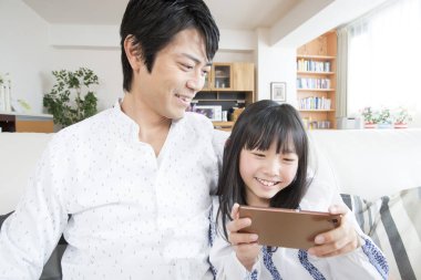 Gülümseyen baba ve kızı evde akıllı telefon kullanıyor.