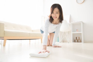 Genç bir kadın temizlik yapıyor, güzel bir Asyalı kız paçavrayla yerleri siliyor.