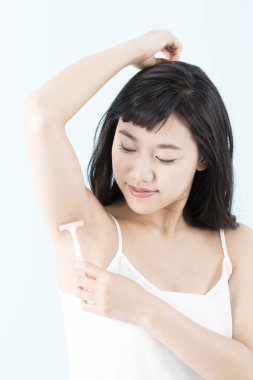 Tüylerini aldırmak için koltuk altını tıraş eden genç bir kadın.