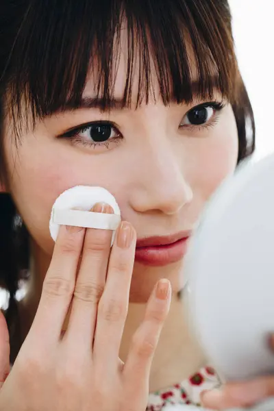young asian woman applying makeup to her face.