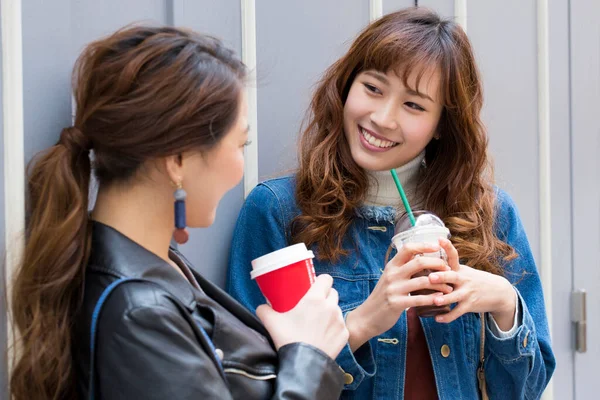 Mutlu genç Asyalı kadınlar kahve içip sohbet ediyorlar.