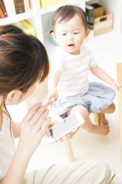 Akıllı telefonlu Asyalı anne ve küçük oğlu birlikte oynuyorlar.