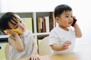 Asyalı çocuklar evde akıllı telefonlardan konuşuyor. 