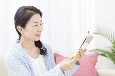 Asyalı kadın evde kitap okuyor. 