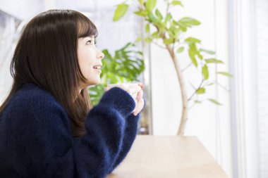 Kafede kahve içen genç Asyalı kadın.