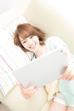 Evde tablet bilgisayar kullanan Asyalı genç kadın, yatakta yatıyor.