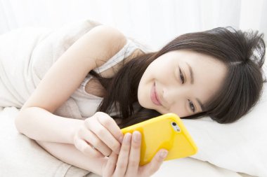 Yatakta cep telefonuyla gülümseyen güzel Asyalı bir kadın.