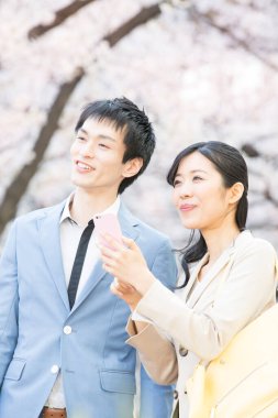 Parkta çiçek açan sakura ağaçları olan genç Asyalı çift.