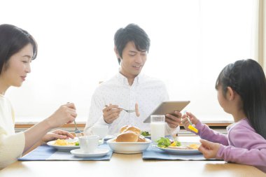 Genç bir aile kahvaltı yapıyor, adam tablet kullanıyor.