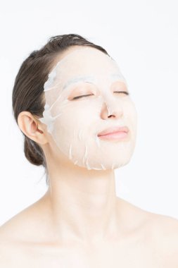 Beyaz arka planda maske takan güzel bir Asyalı kadın. Cilt bakımı kavramı