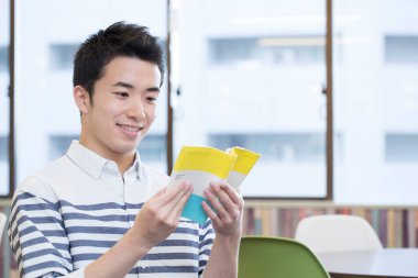 Asyalı öğrenci üniversitede masada okuyor. 