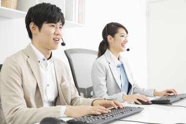 İki genç Asyalı iş adamı ofiste kulaklık takıyor. 