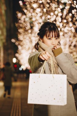 Sonbahar kıyafetleri içinde güzel bir Japon kadın alışveriş torbalarıyla sokakta oturuyor, aydınlanmış bir şehir geçmişi var. 