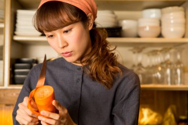 Asyalı genç bayan garson mutfakta havuç soyuyordu.