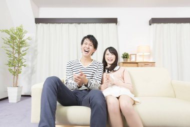 Genç Asyalı çift evde televizyon izliyor.