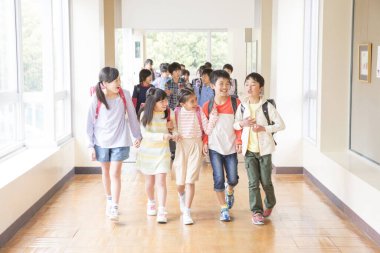 Okul koridorunda sırt çantalı bir grup Japon çocuk yürüyor. 