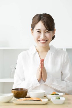 Dua eden bir kadın, her iki elini de yemek masasında bir araya getiriyor. 