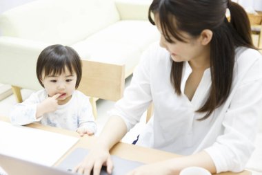 Genç anne ve küçük kızı evde dizüstü bilgisayar kullanıyorlar.