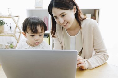 Asyalı anne ve küçük kızı evde dizüstü bilgisayar kullanıyorlar.