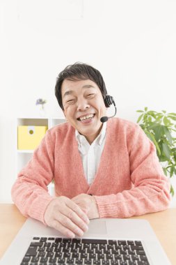 Evde çalışan kulaklıklı ve laptoplu Asyalı bir adam.
