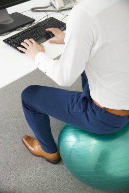 İş adamı bilgisayarda çalışıyor ve ofisteki topun üzerinde oturuyor.