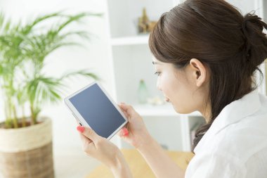 Genç Asyalı kadın oturma odasında tablet kullanıyor.