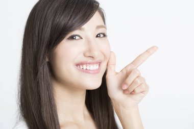 Genç ve güzel bir Japon kadın, beyaz arka plandaki kamerayı işaret ediyor. 