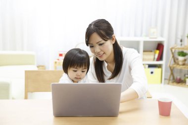 Genç anne ve küçük kızı evde dizüstü bilgisayar kullanıyorlar.