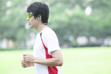 Genç yakışıklı Asyalı adam parkta koşuyor. 