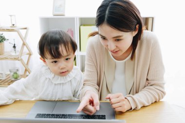 Asyalı anne ve küçük kızı evde dizüstü bilgisayar kullanıyorlar.