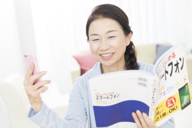 Bir mesaj okurken kitap okuyan Asyalı genç kadın. 