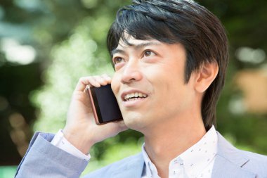 Genç Asyalı işadamı dışarıda cep telefonuyla konuşuyor.