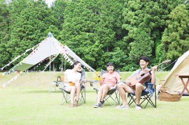 Mutlu Asyalı arkadaşlar kamp parkında müzik aletleri çalıyorlar.