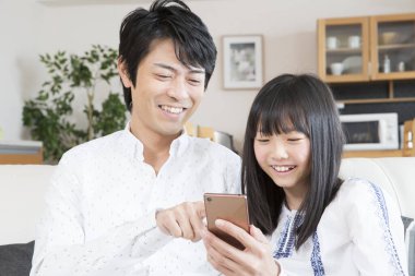 Gülümseyen baba ve kızı evde akıllı telefon kullanıyor.