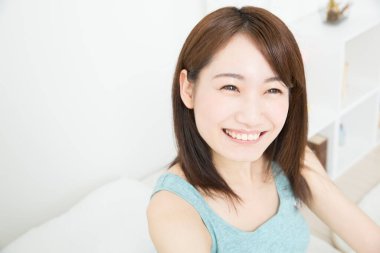 Gülümseyen Asyalı kadın yatakta oturuyor.