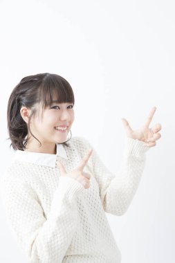 Beyaz kazaklı genç Japon kadın beyaz stüdyo geçmişini işaret ediyor.