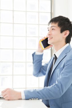 Ofiste telefonla konuşan genç Japon iş adamının yakın plan portresi.