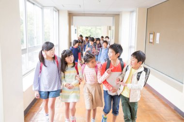 Okul koridorunda sırt çantalı bir grup Japon çocuk yürüyor. 