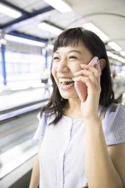 Tren istasyonunda cep telefonu olan genç Asyalı kadın.