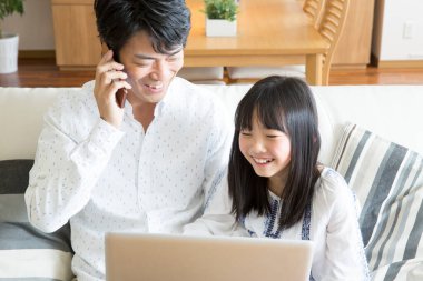 Genç Asyalı baba ve kızı evde dizüstü bilgisayar kullanıyor.