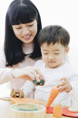 Asyalı anne ve oğlu evde tahta oyuncaklarla oynuyorlar. 