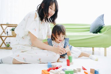 Evdeki oturma odasında annesiyle oynayan tatlı Asyalı küçük kız.