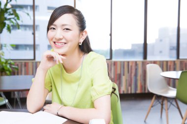 Genç, güzel Asyalı kadın ofiste oturuyor ve gülümsüyor.