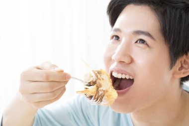 Genç Asyalı adam pasta yiyor. 