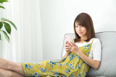 Genç Asyalı kadın evde dinlenirken akıllı telefondan mesaj okuyor.