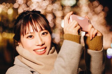 Kadın gece akıllı telefonuyla fotoğraf çekiyor.