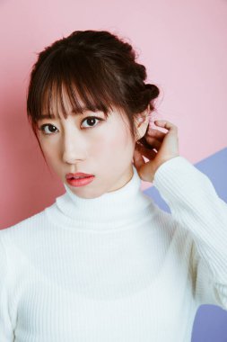 Pembe arka planda süveteri olan güzel bir Asyalı kadın.