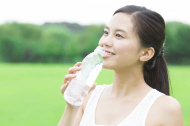 Yeşil yaz parkında gündüz vakti su içen güzel Japon kadın. 