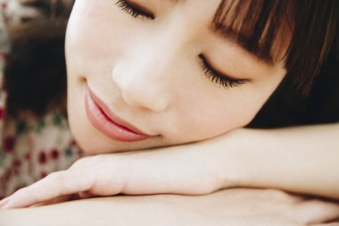 Gözleri kapalı genç bir kadın elleri üzerinde yatıyor. 