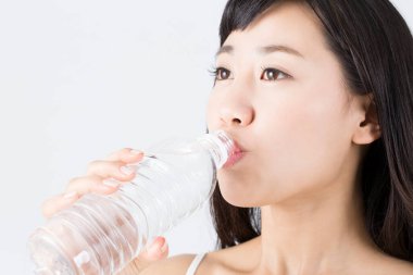 Genç Asyalı kadın şişeden su içiyor. 